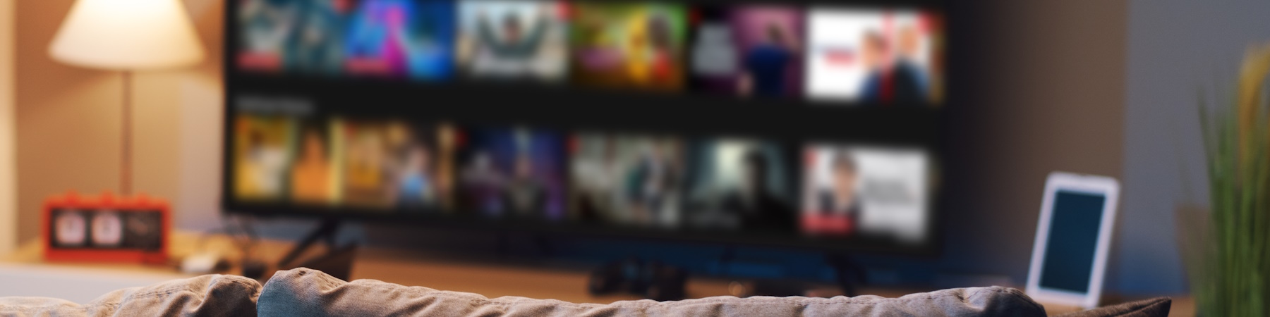 Fotografi som viser interiøret i en stue. I forgrunnen skimtes ryggen på en sofa. I bakgrunnen kan vi se en stor  TV-skjerm med mange apper.