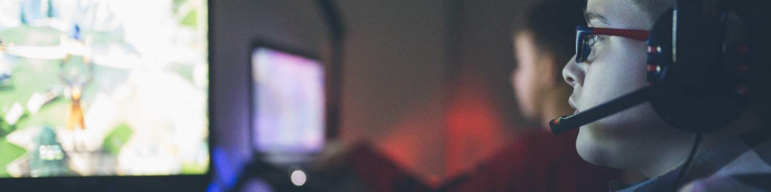 Fotografi av to gutar som spelar dataspel. Den næraste guten har på seg briller og eit gaming-hovudsett med mikrofonbom.