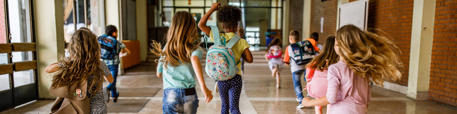 Fotografi av ni skolebarn som spring i ein korridor. Det er både gutar og jenter i gruppa, og fleire av dei har på seg skolesekkar.