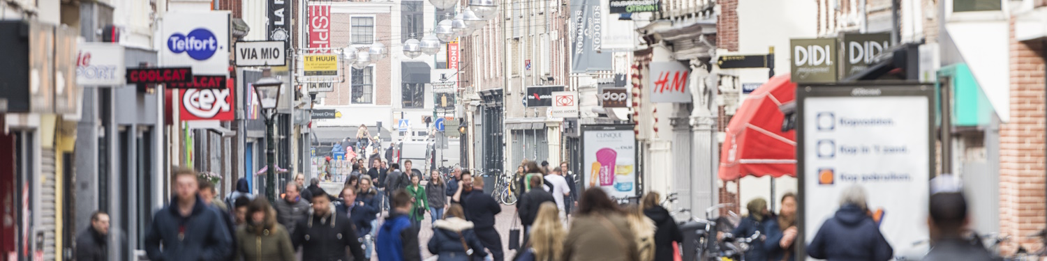 Fotografi av ei travel gågate på dagtid. Butikkane på kvar side av gata har reklameskilt og plakatar av alle slag.